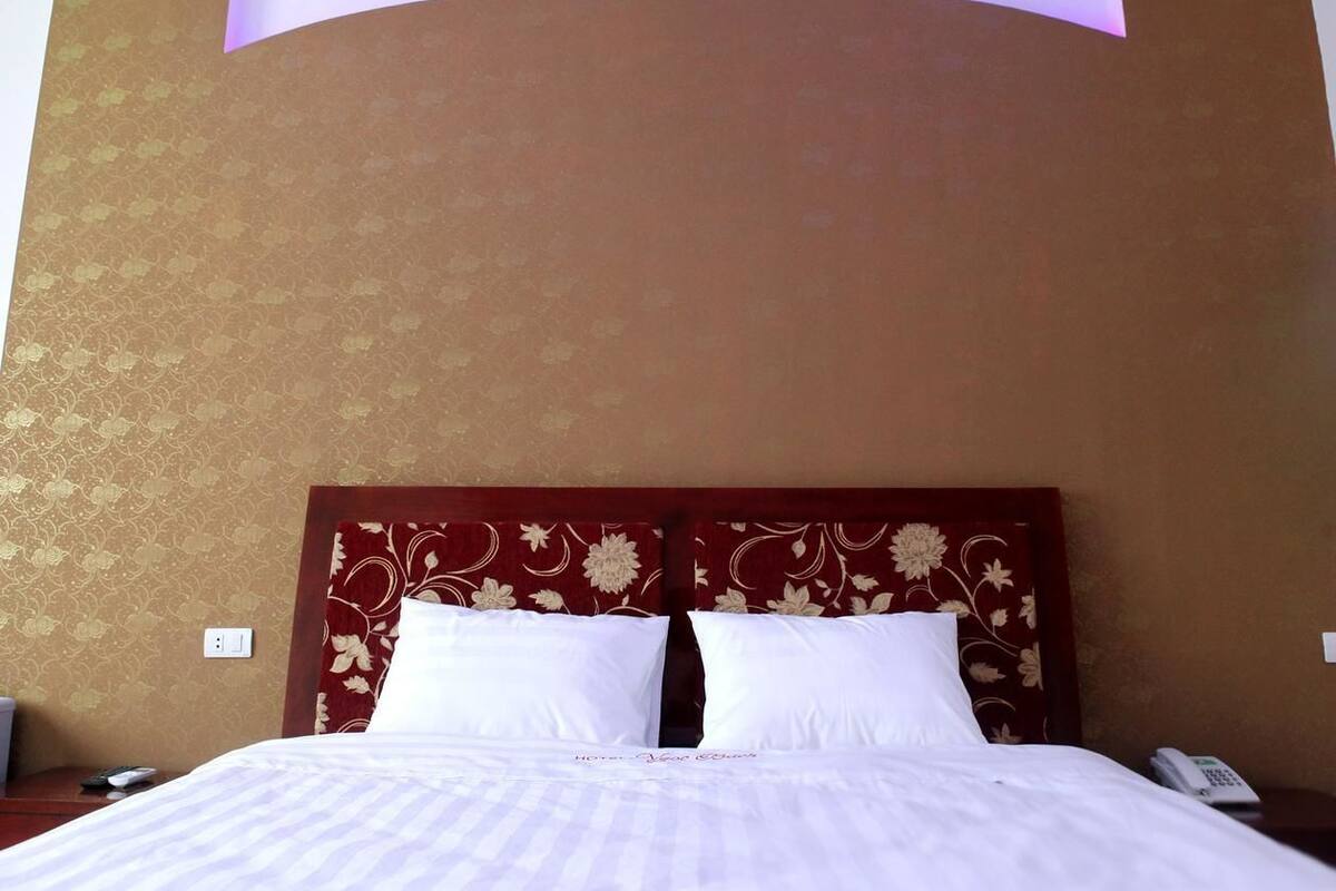 Quarto de hotel com uma cama grande, cabeceira de madeira com padrões florais e luminária fixada na parede.