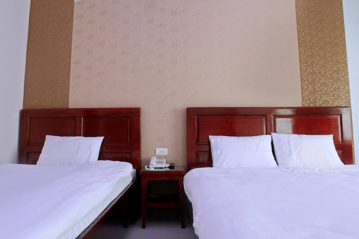 Quarto de hotel com duas camas de solteiro, cabeceiras de madeira, lençóis brancos e mesa de cabeceira com telefone.