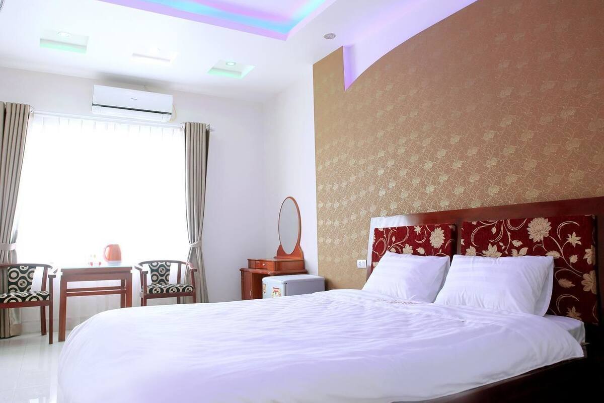 Quarto de hotel com uma cama grande, uma escrivaninha com cadeira, ar condicionado e uma janela com cortinas.