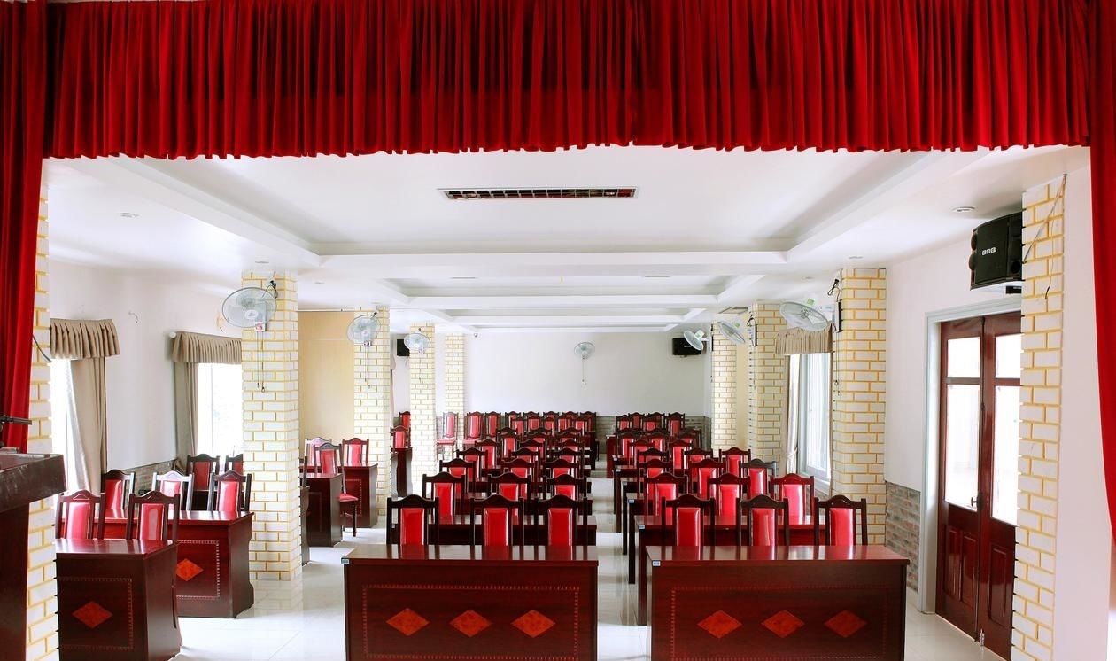 A conference room with rows of chairs, a stage with a red curtain, and brick walls.