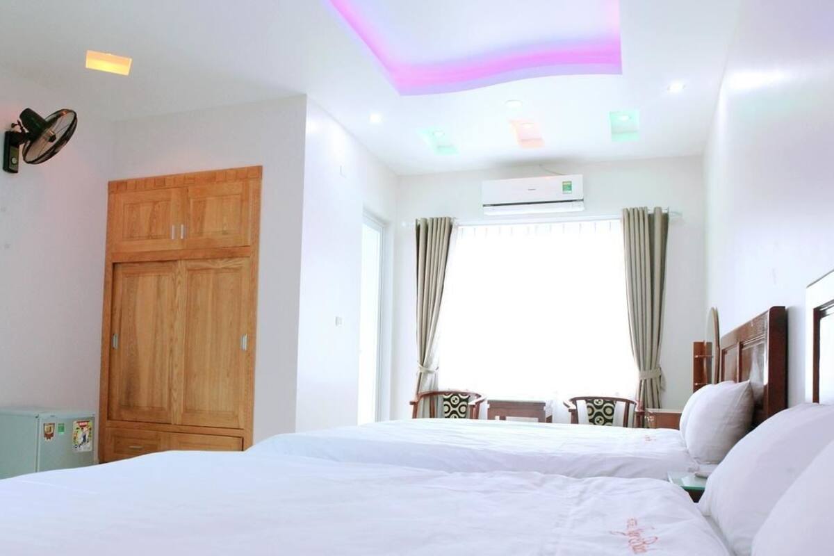 Um quarto com cama, guarda-roupa, janela com cortinas, ventoinha no teto e ar condicionado.