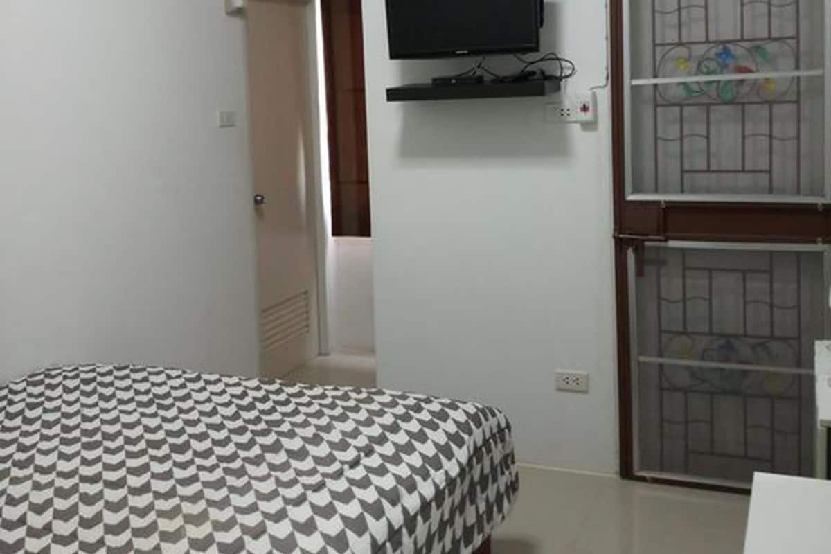 A bedroom with a bed, a mounted TV, and a window with a metal grill.