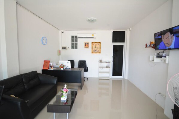 Un salon moderne avec un canapé en cuir noir, une table basse en verre, un bureau avec un ordinateur et un téléviseur fixé au mur.