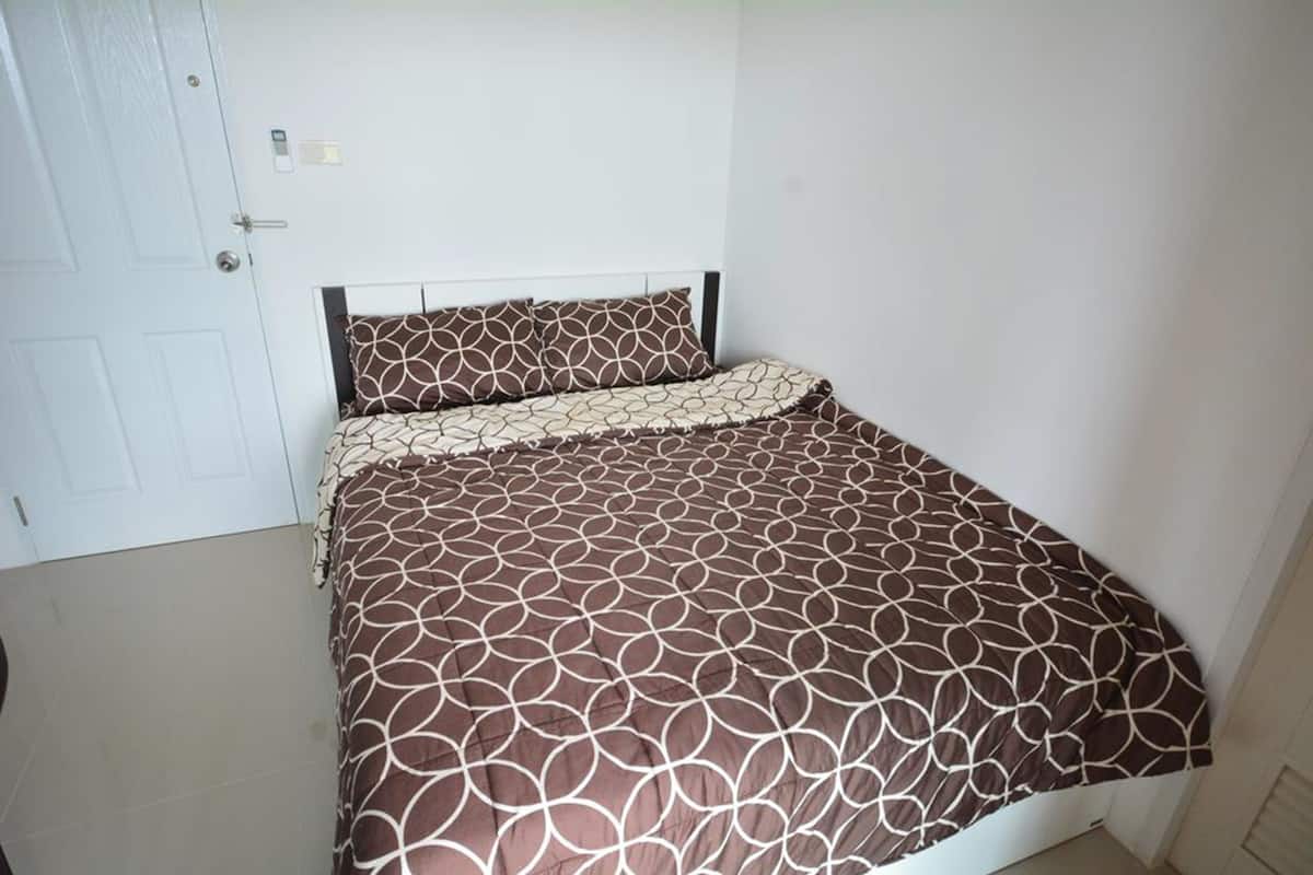 A single bed with a patterned bedspread and matching pillow in a room with white walls and a door.