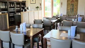 A restaurant with wooden beams, tables with chairs, a bar area with bottles, and a large window. - Landhaus vor Burg Eltz (Wierschem)