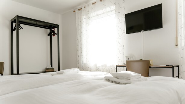 Une chambre d’hôtel avec deux lits, un bureau, une chaise, une télévision et une fenêtre avec des rideaux.