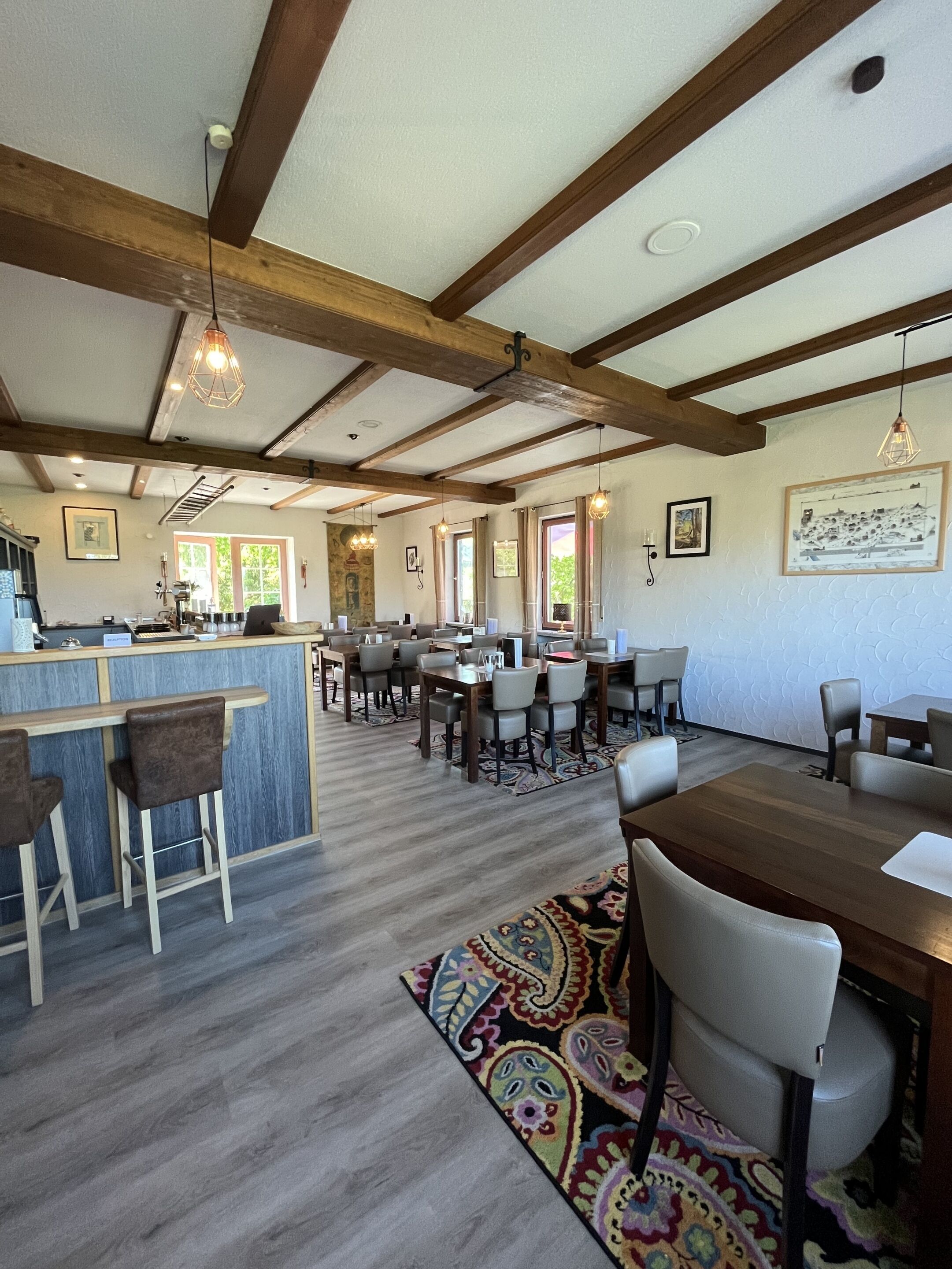 A spacious dining area with wooden beams, a bar, and a patterned rug.