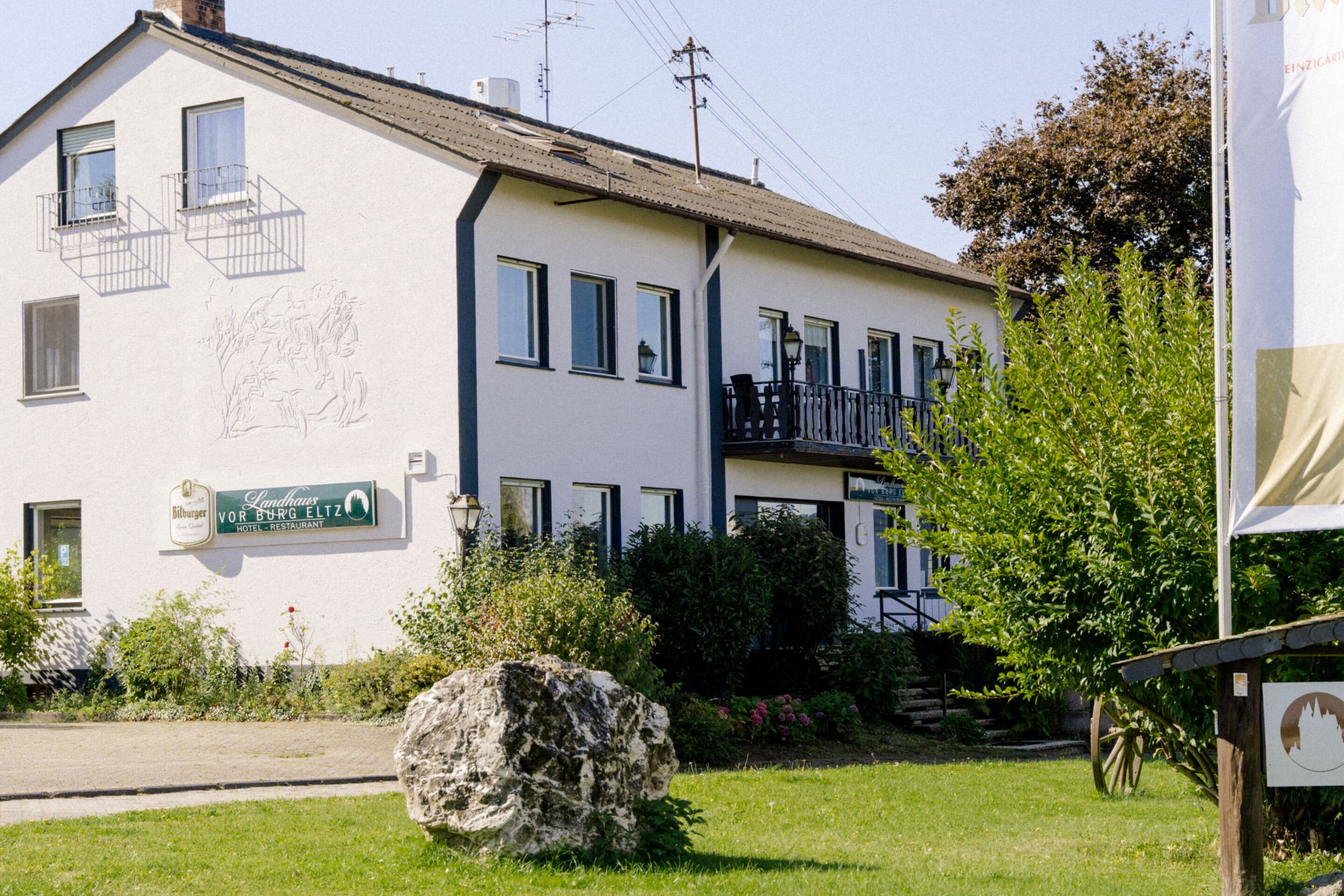 A hotel with a balcony, a large rock in the front yard, and a sign indicating it's a hotel and restaurant.
