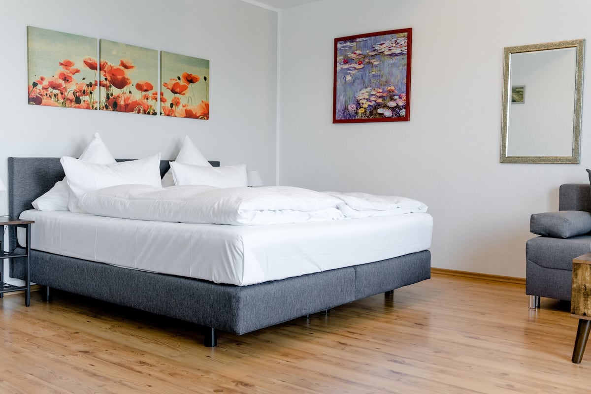Un dormitorio moderno con una cama tapizada en gris, ropa de cama blanca, suelo de madera y obras de arte en las paredes.