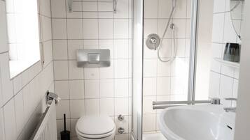 Un baño moderno con inodoro, lavamanos, ducha y una toalla en el suelo.