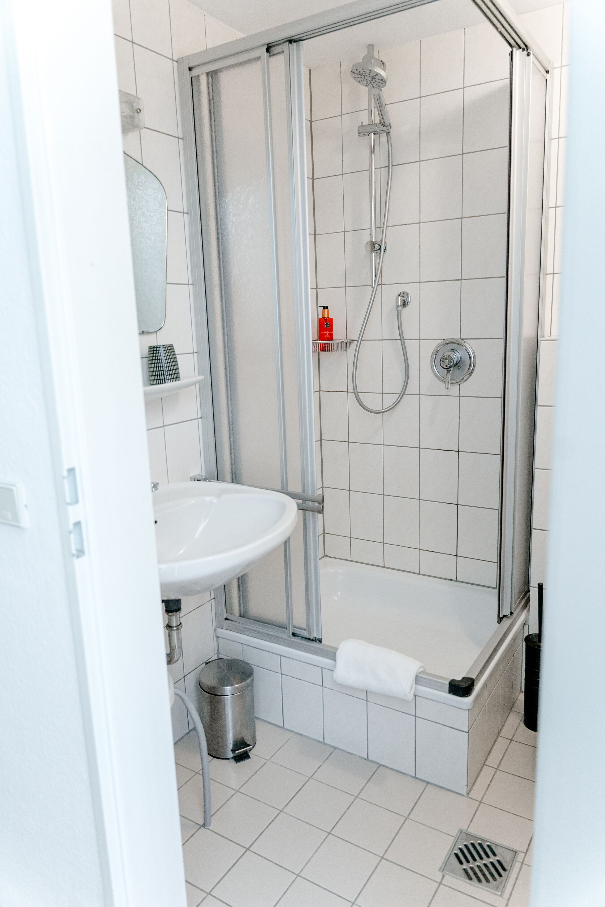 A modern bathroom with a glass-enclosed shower, a white sink, and a small trash bin.
