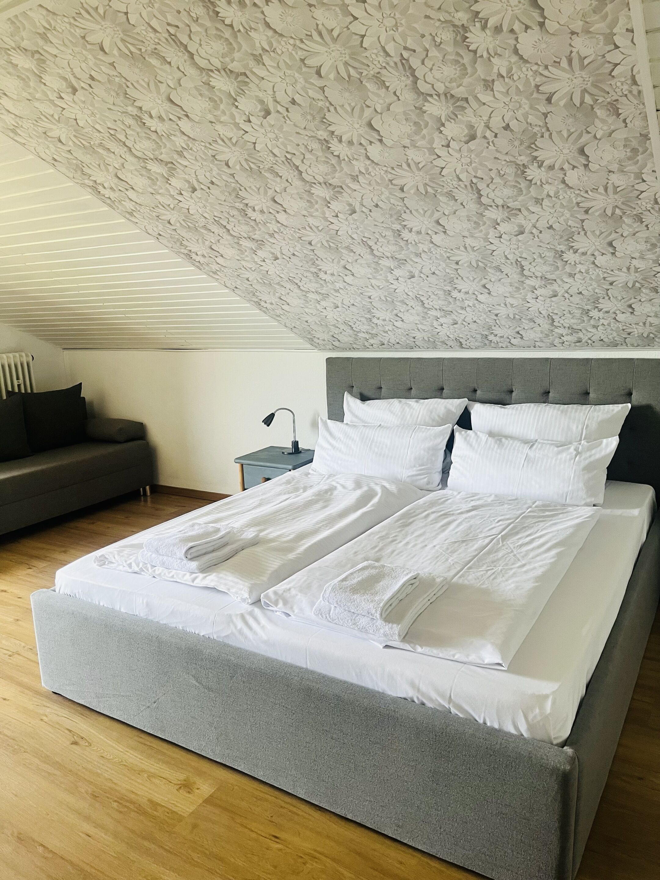 A bedroom with a large bed, a grey headboard, and a floral ceiling design.