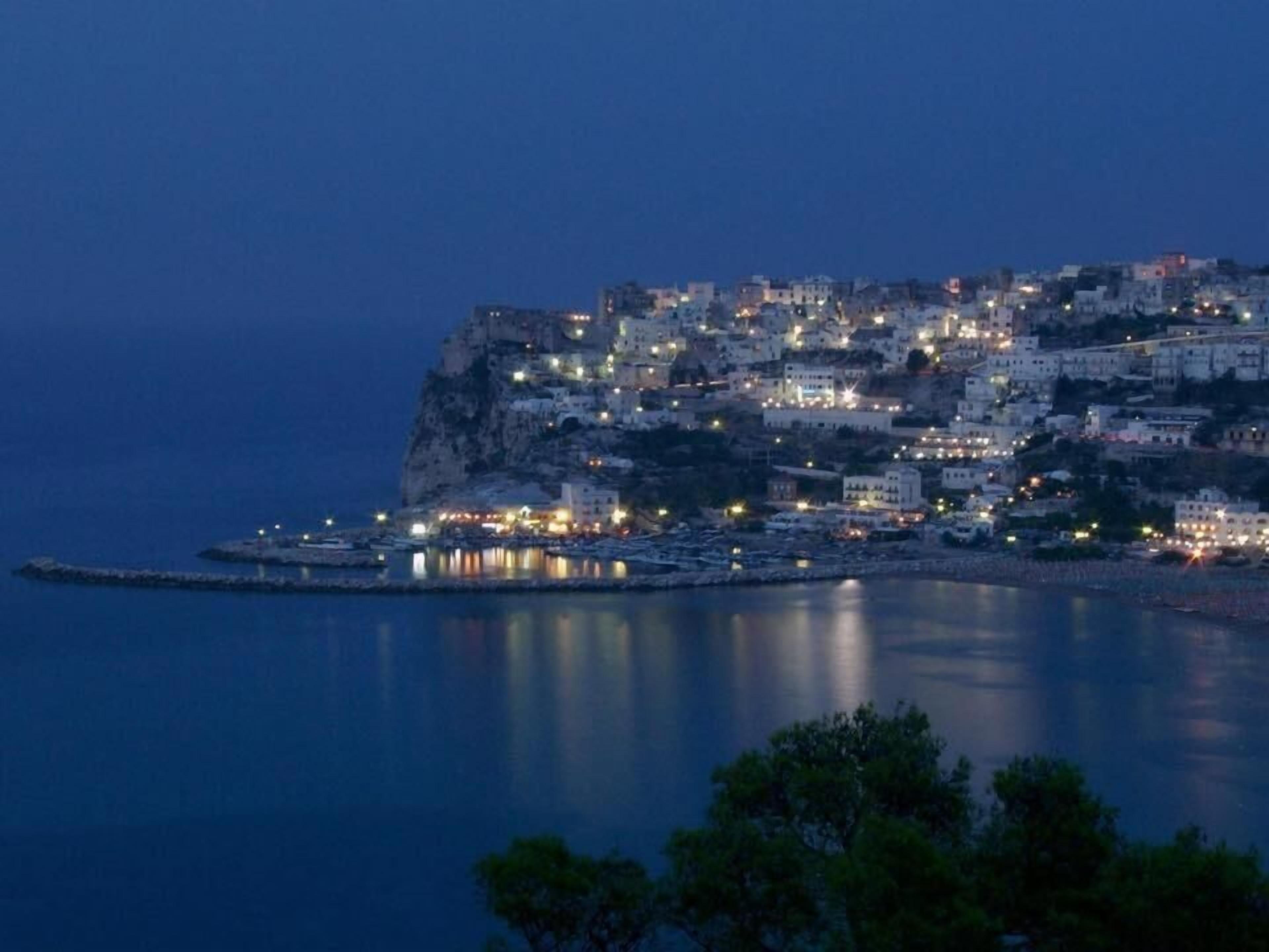 Un pueblo costero al anochecer, con edificios sobre un acantilado con vistas al mar.