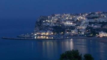 Un pueblo costero al anochecer, con edificios sobre un acantilado con vistas al mar.