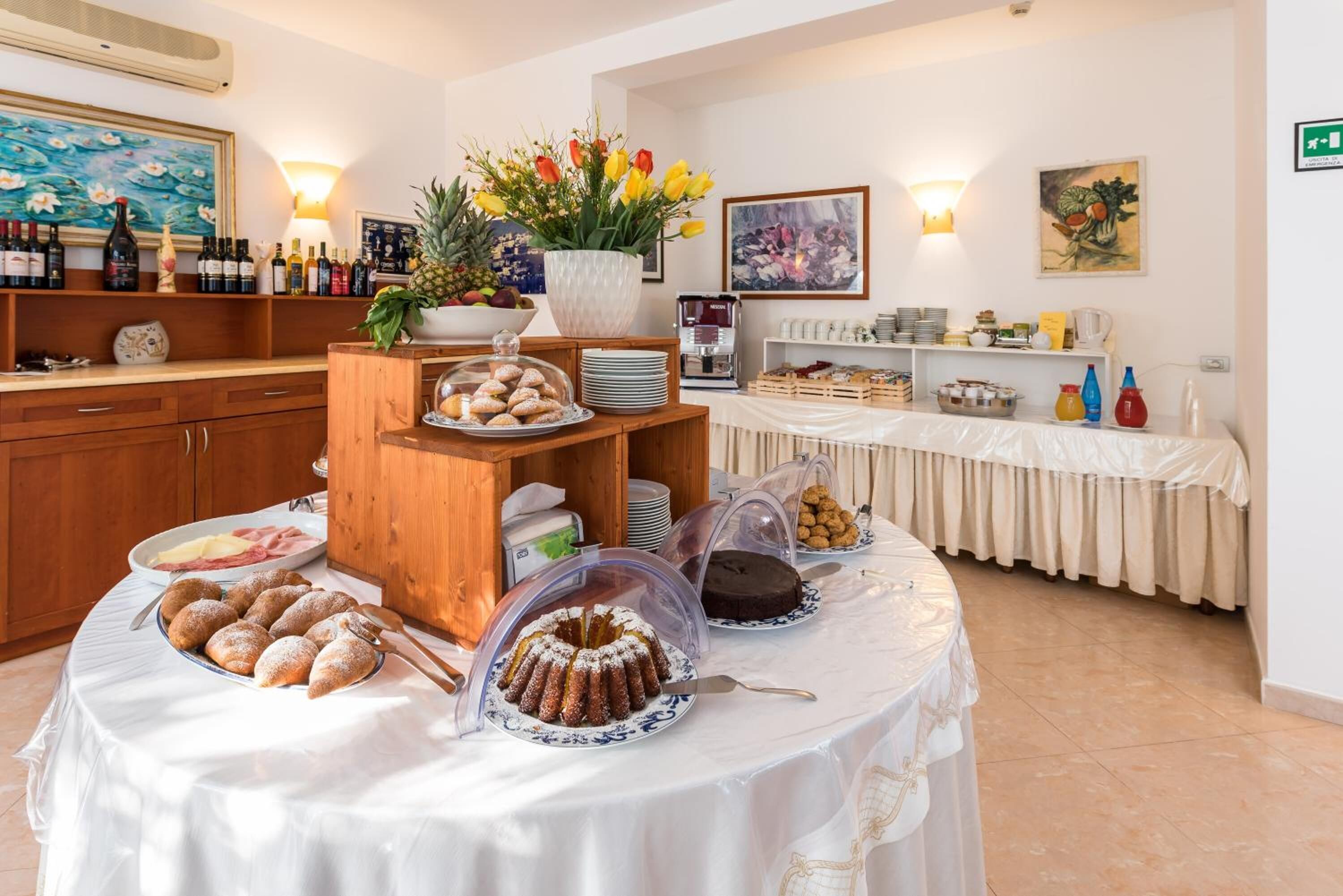Mesa de buffet con diversos pasteles y postres, una máquina de café y un centro de mesa floral.