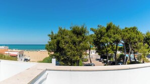 A coastal view with a clear sky, a beach, and a parking area with trees.