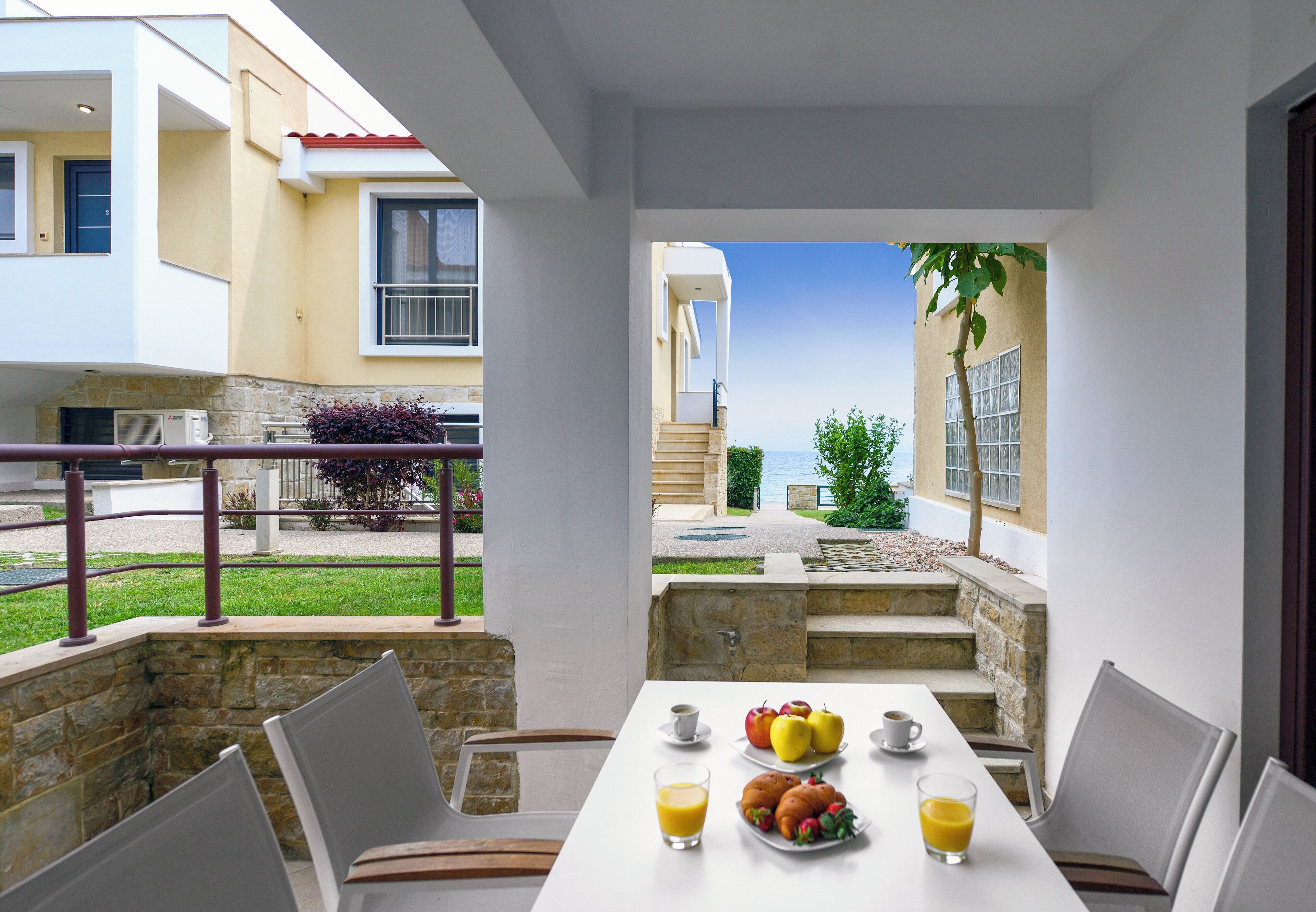 A dining area with a table set for breakfast, outdoor seating, and a view of the sea.