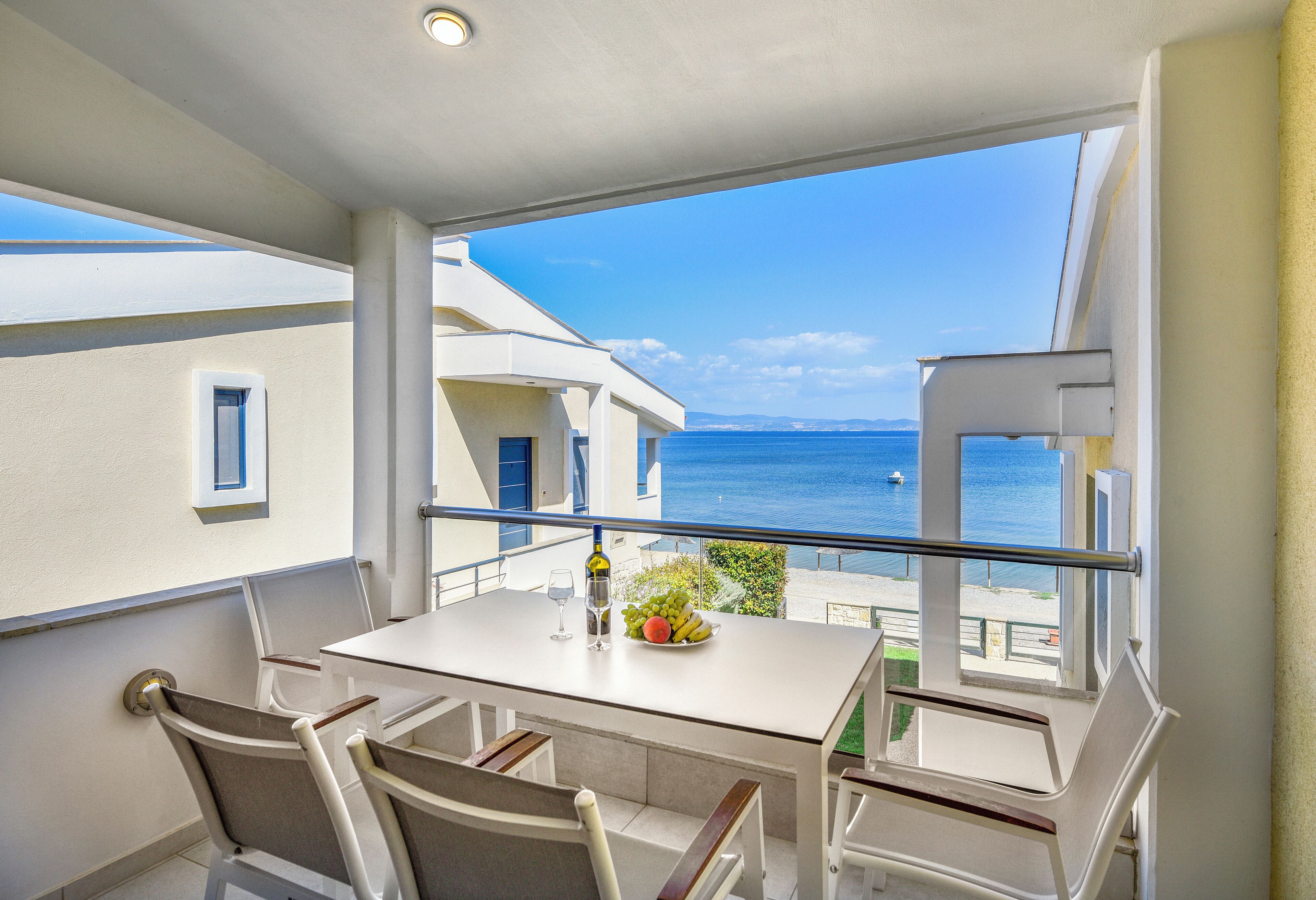 A balcony with a white table and chairs, a bottle of wine, and a fruit bowl.