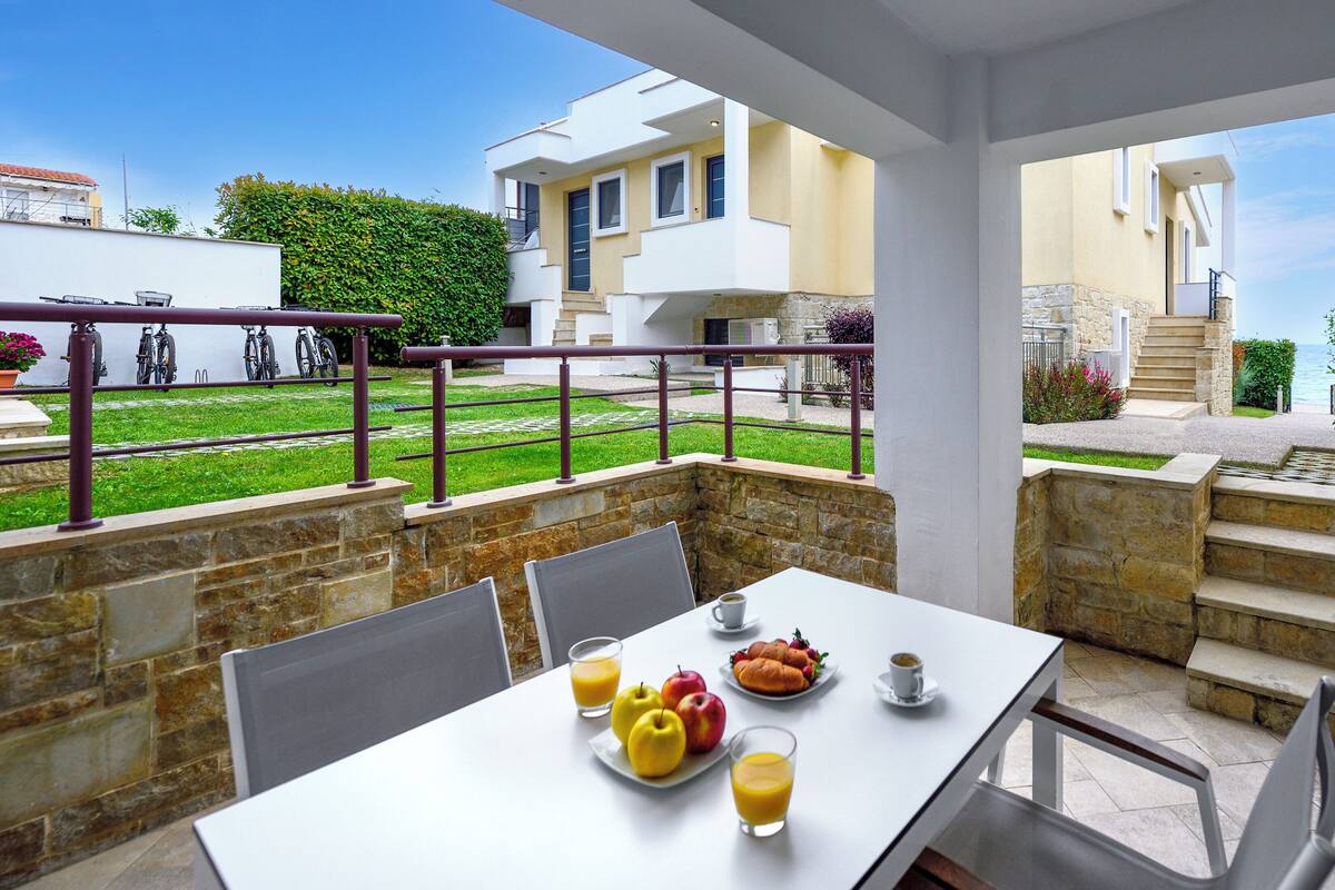 Un coin repas avec une table dressée pour le petit-déjeuner, des sièges à l’extérieur et une vue sur la mer.