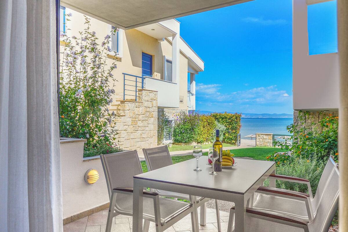 Une terrasse extérieure avec une table et des chaises, une bouteille de vin et une vue sur la mer.