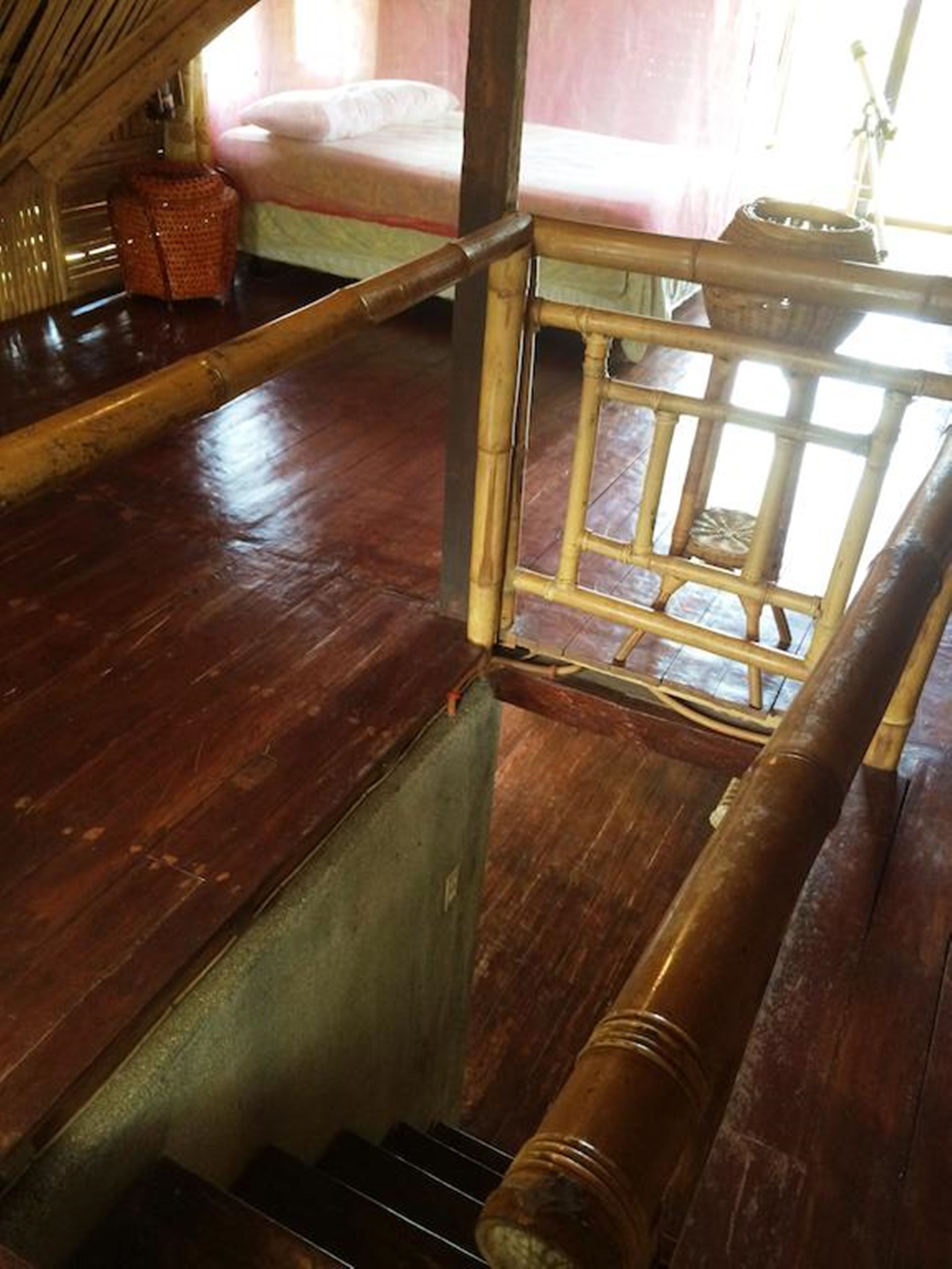Uma escada de madeira com corrimão de bambu leva a um quarto com cama e janela.