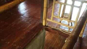 Uma escada de madeira com corrimão de bambu leva a um quarto com cama e janela.