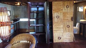 Een kamer met een houten plafond, een bamboepartition, een rieten stoel en een wastafel.