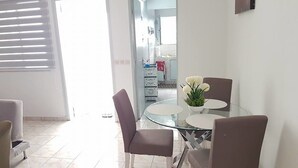 A dining area with a glass table and four chairs, a white wall, a door, and a small plant on the table. - Résidence Petite Villa (Abidjan)