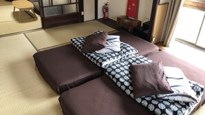 Ett traditionellt japanskt rum med tatamimattor på golvet, ett lågt bord och en futonmadrass med mönstrat sänglinne.