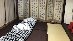 Ett traditionellt japanskt rum med tatamimattor på golvet, en futonmadrass, en shojiskärm med kalligrafi och en futon placerad direkt på golvet.