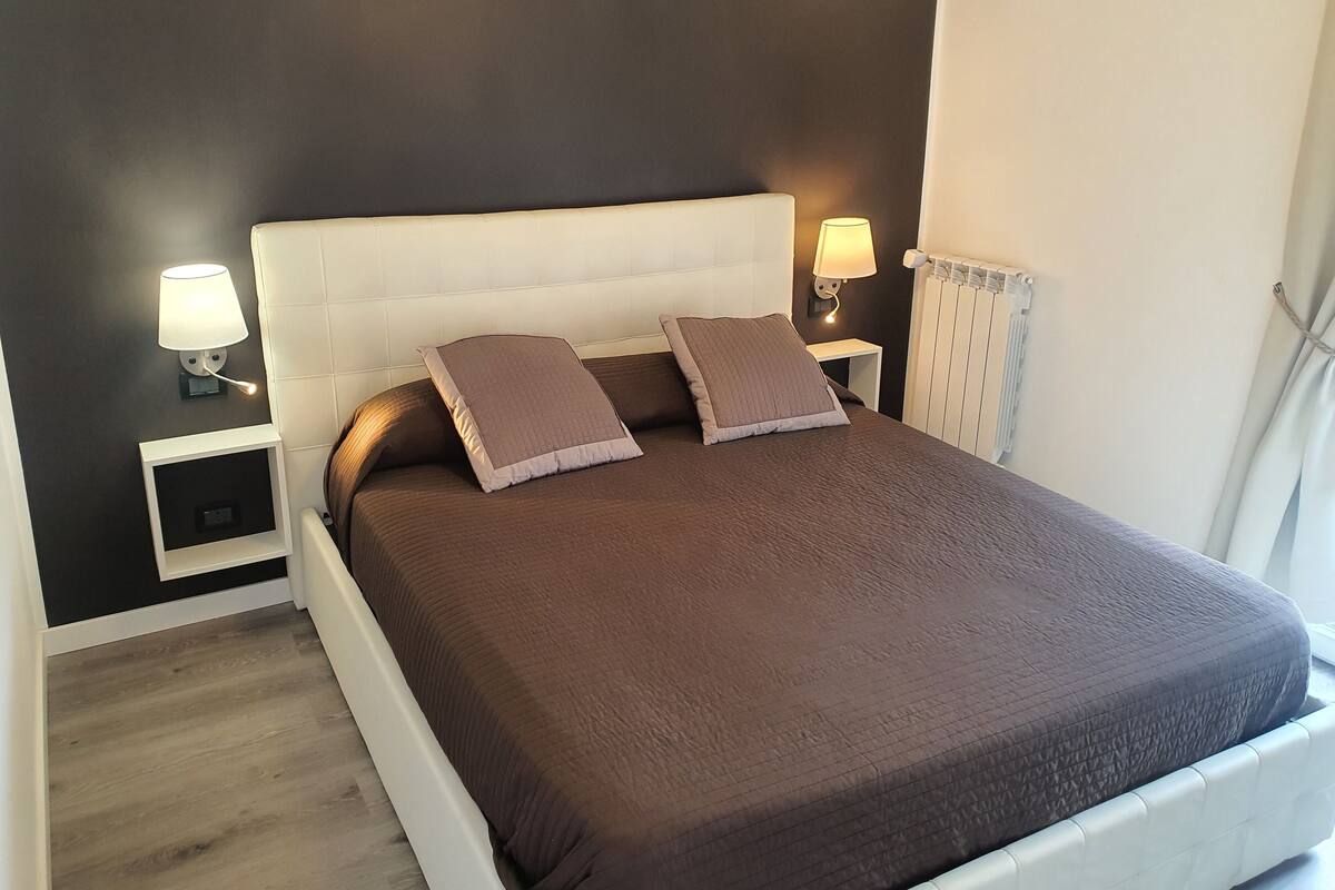 Un lit bien fait, avec une couverture marron, deux oreillers et deux lampes de chevet.