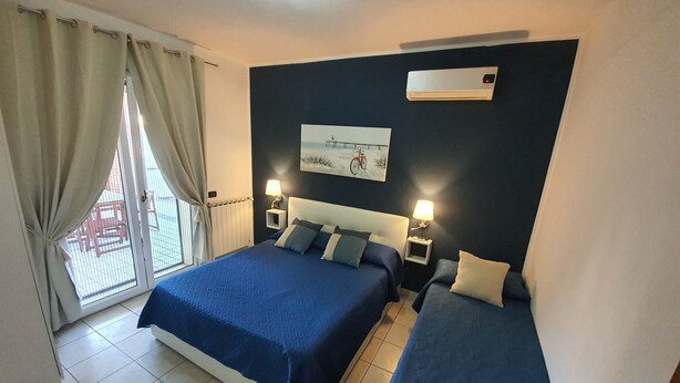 A hotel room with two beds, a window with curtains, a radiator, and a wall-mounted air conditioner. - Guest House Brezza Marina (Fiumicino)