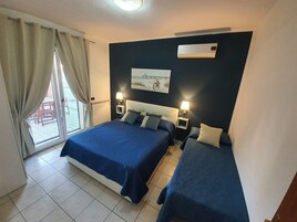 Camera d'albergo con due letti, una finestra con tende, un termosifone e un condizionatore d'aria a parete.