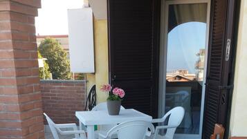 Une terrasse avec une table et des chaises blanches, une plante en pot et un pilier en briques.