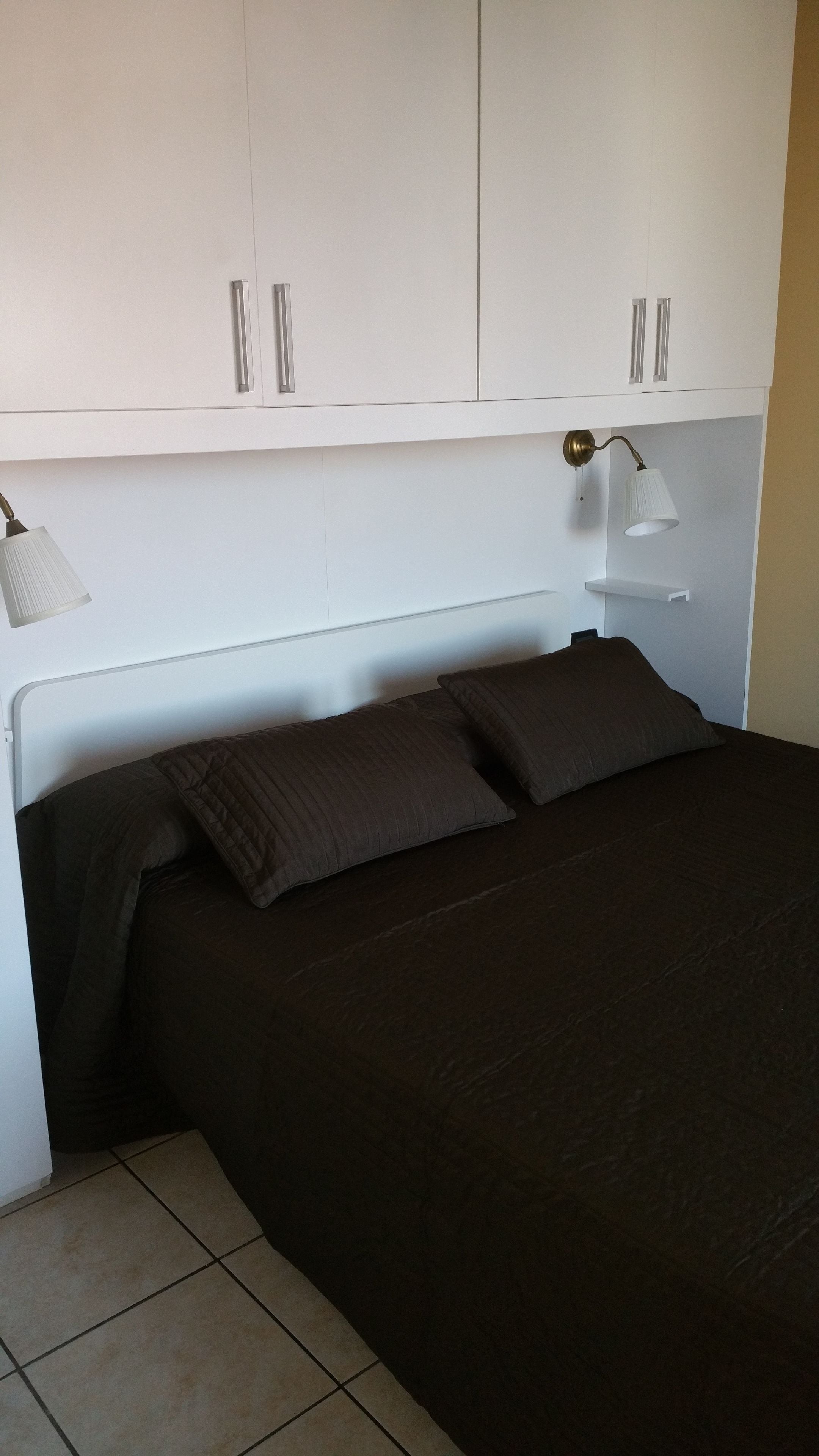 Une chambre à coucher avec un lit, deux oreillers, une table de chevet, une lampe et une armoire.