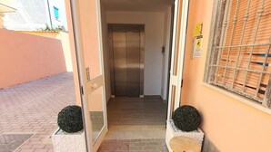An entrance with a door leading to an elevator, a small wooden stool, and two potted plants. - Guest House Brezza Marina (Fiumicino)