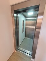 Un ascensore con interni in metallo, un pannello di controllo con pulsanti e un lampadario a soffitto.