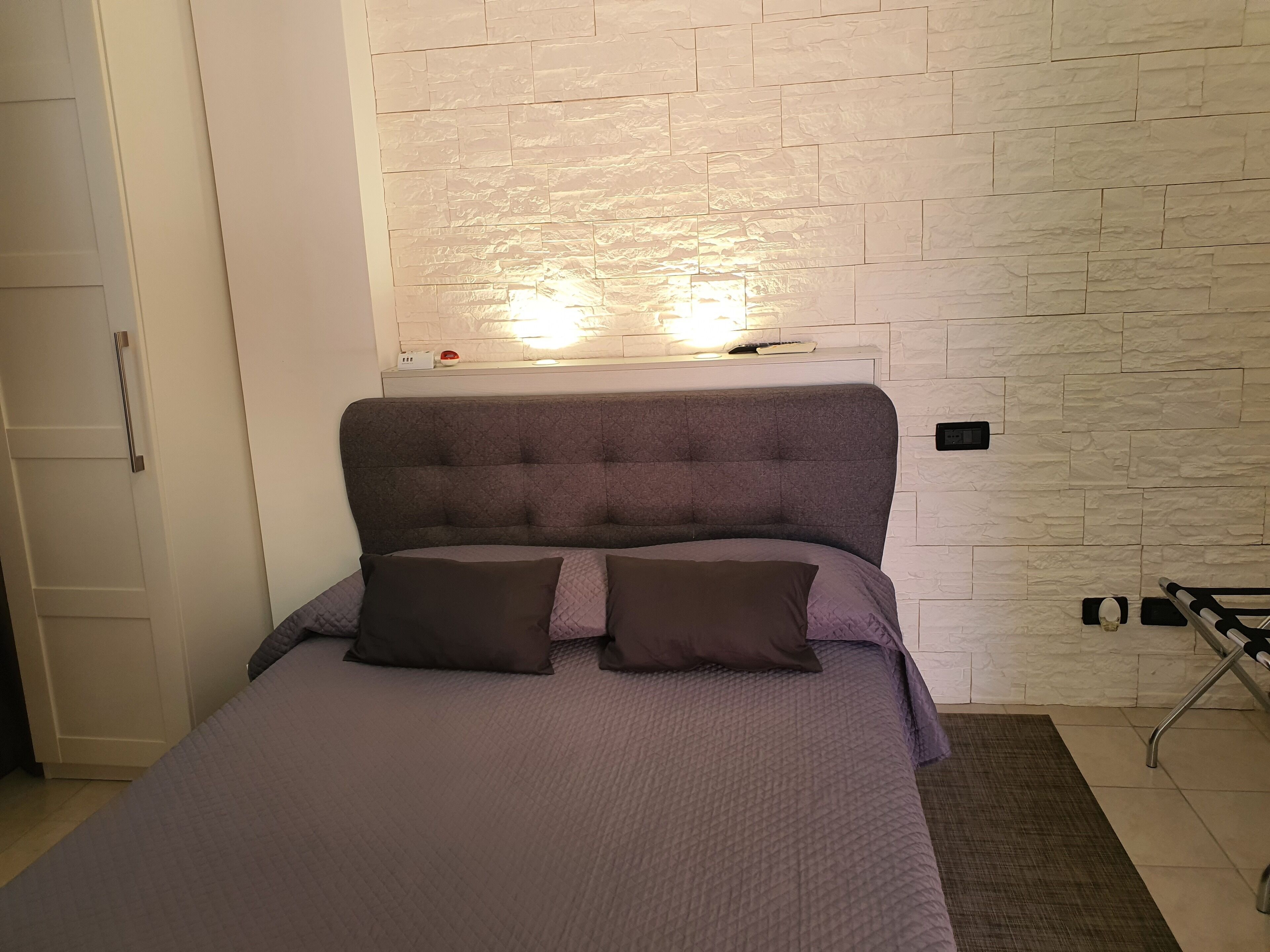 Une chambre à coucher avec un lit, des oreillers, une table de chevet et un luminaire fixé au mur.