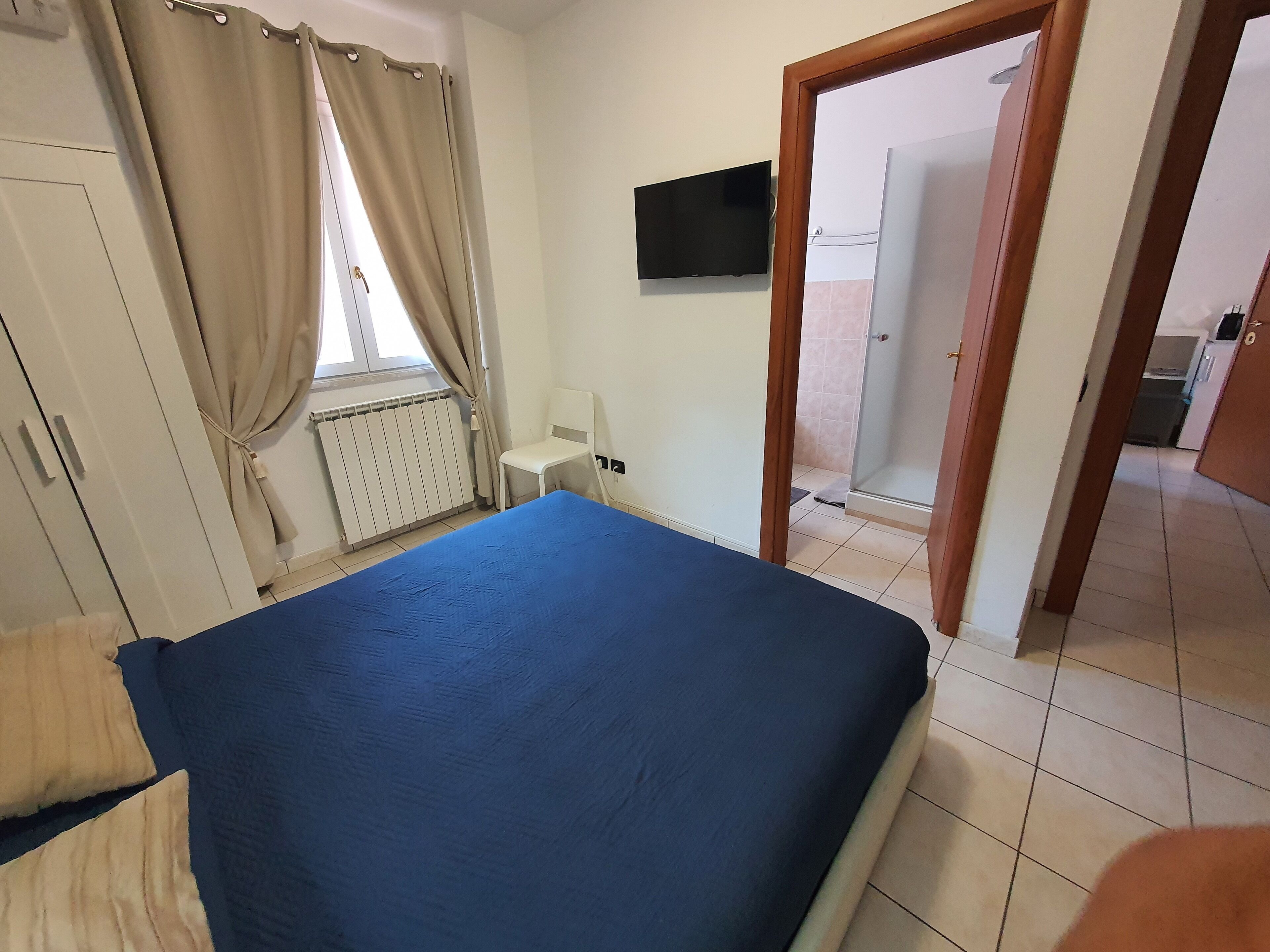 Een slaapkamer met een bed, een stoel, een televisie en een badkamer die door een geopende deur zichtbaar is.