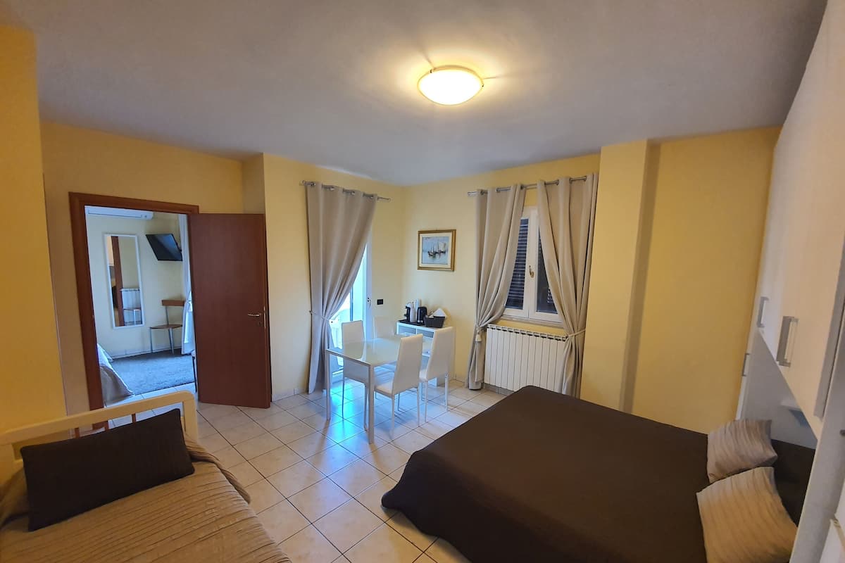 Une chambre d’hôtel avec un lit, un bureau et une chaise. Il y a une fenêtre avec des rideaux, un radiateur et un tableau au mur.