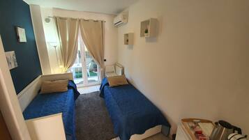A small, well-lit room with two beds, a small table, and a kitchenette.