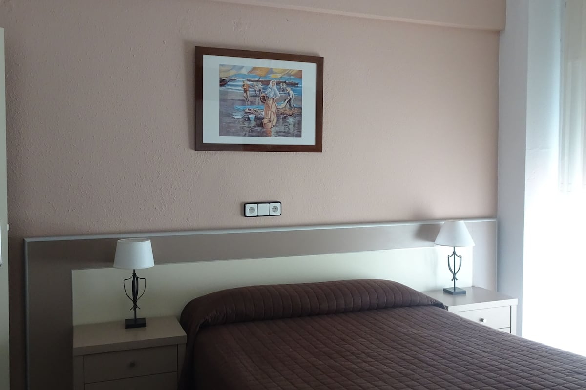 A hotel room with a large bed, two bedside tables with lamps, a framed picture on the wall, and a headboard with a control panel.