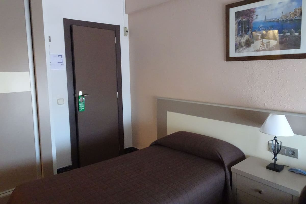 A hotel room with a bed, a nightstand, a lamp, a painting, and a door with a lock.