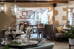 A restaurant with tables set for dining, a stone wall, and a cozy seating area with cushions. - The Black Horse Hotel Grassington (Skipton)