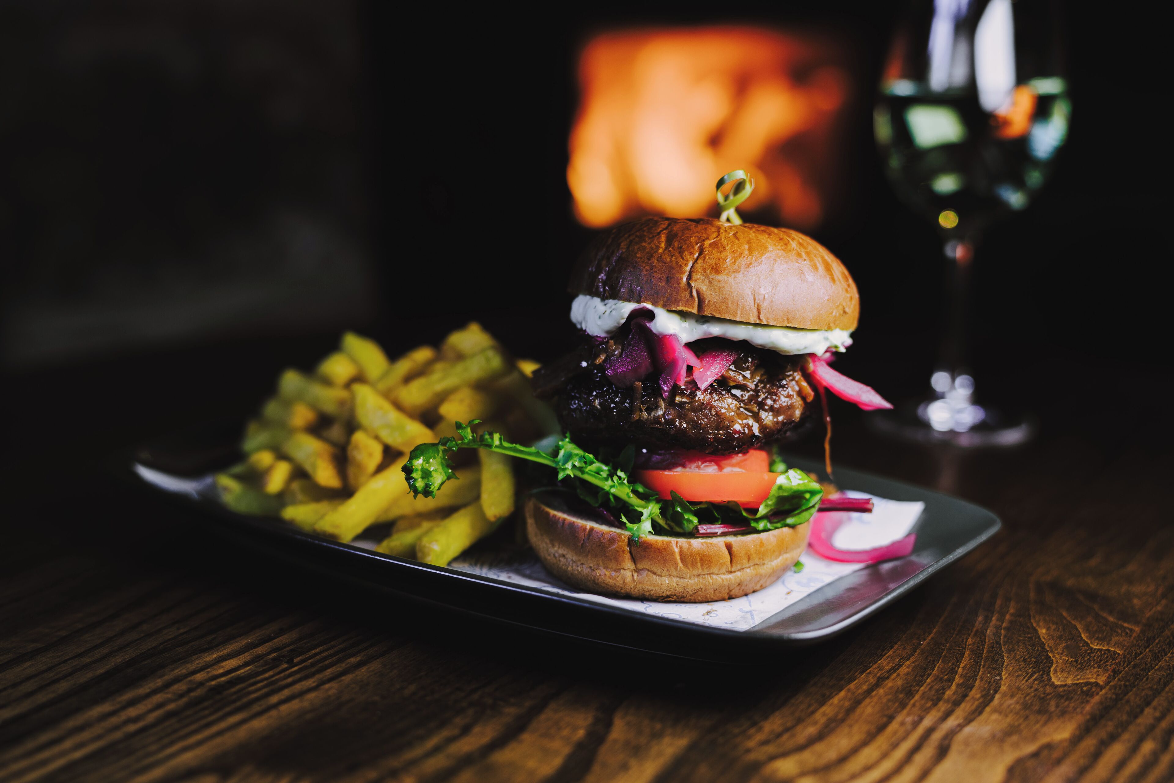 A burger with fries and a glass of wine on a wooden table.