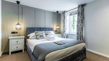 Een slaapkamer met een groot bed, twee nachtkastjes, een lamp en een raam met gordijnen.