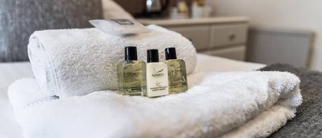 Una cama bien hecha con una toalla doblada y tres botellas de gel de ducha.