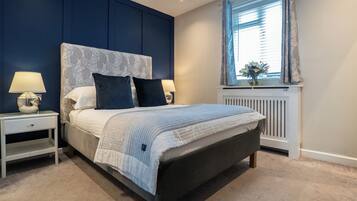 Un dormitorio con cama, dos mesitas de noche, un radiador y una ventana con cortinas.