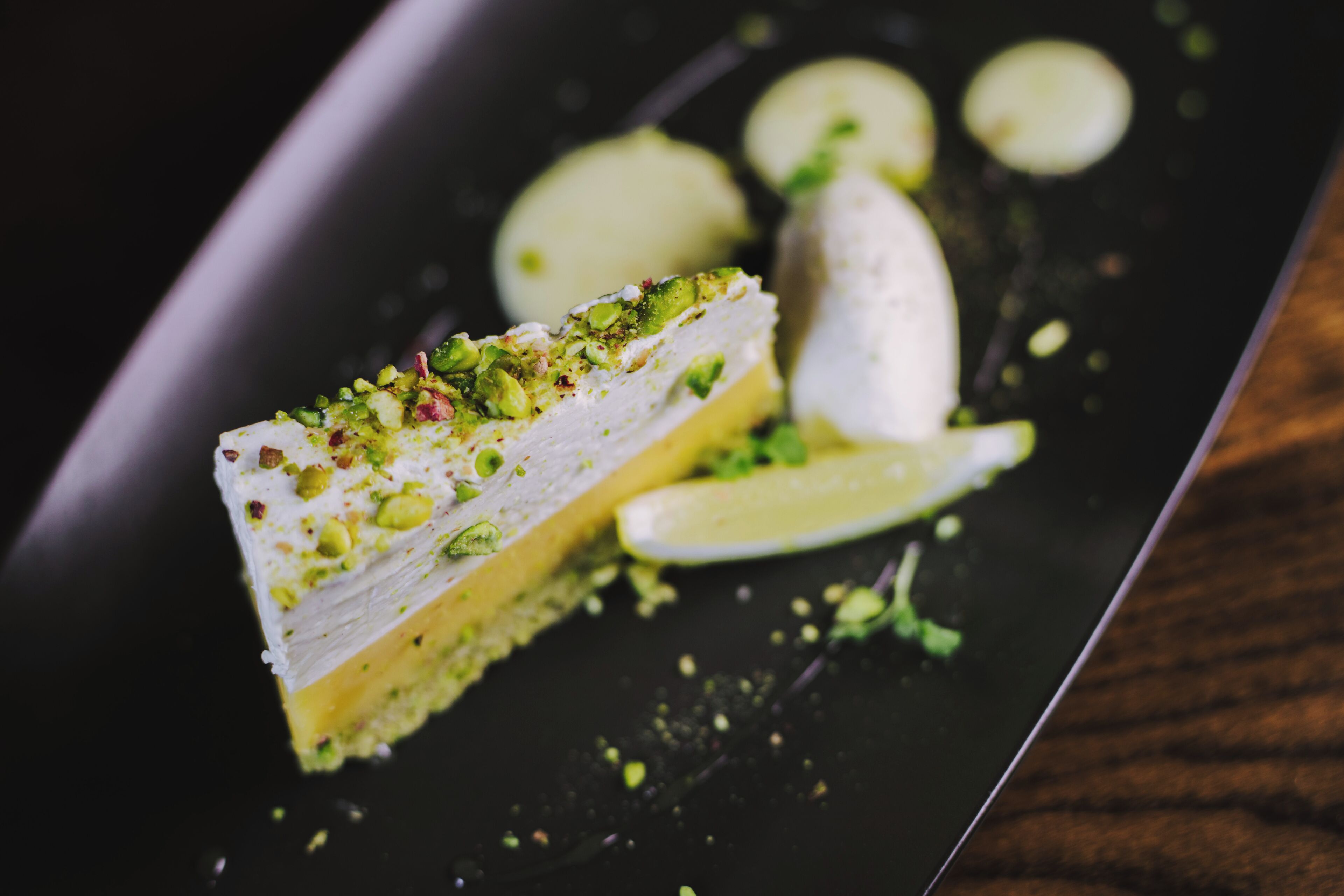 Una porción de postre en capas con pistachos sobre un plato oscuro.
