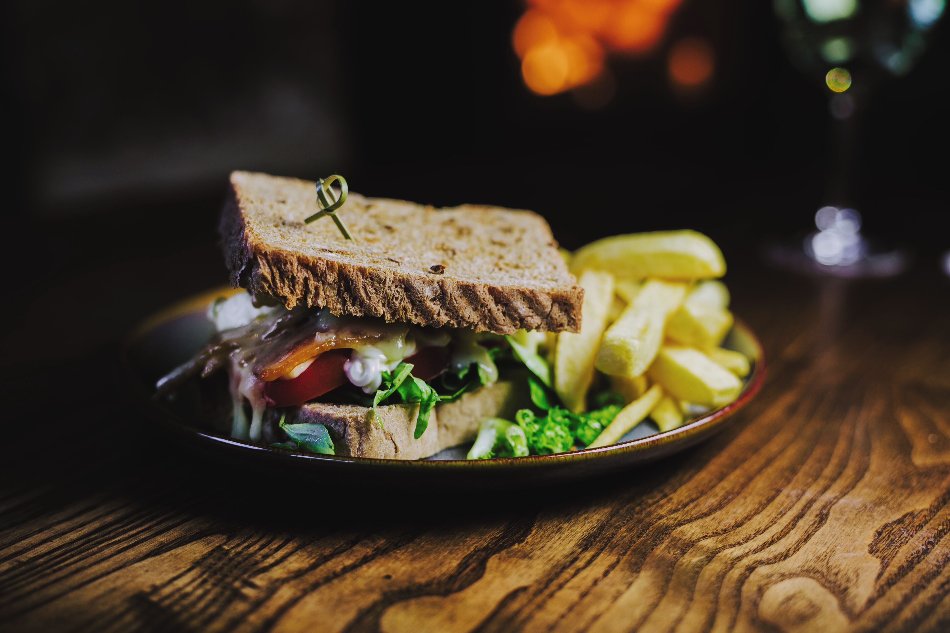 A sandwich with a toothpick on a plate, accompanied by fries and a glass of water on a wooden table.